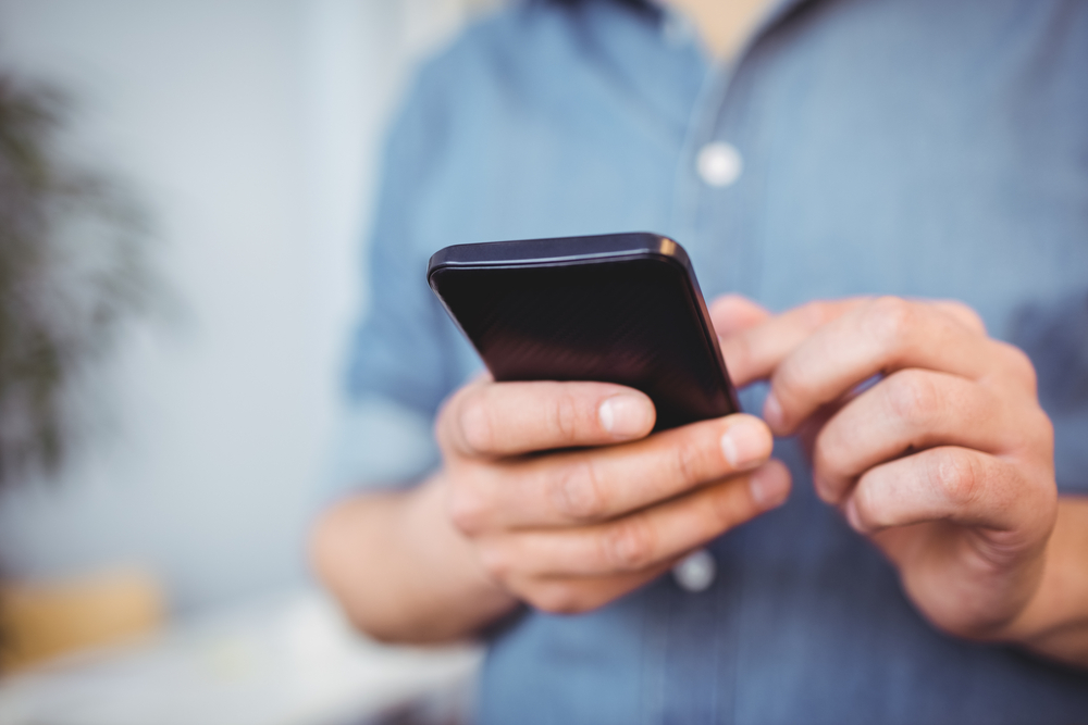 Midsection of businessman texting on cellphone while standing at creative office